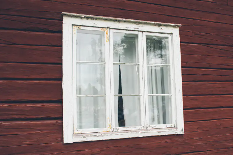 Casement Windows in Newcastle upon Tyne White casement window with net curtains in a dark red timber wall, illustrating casement windows for homes in Newcastle upon Tyne