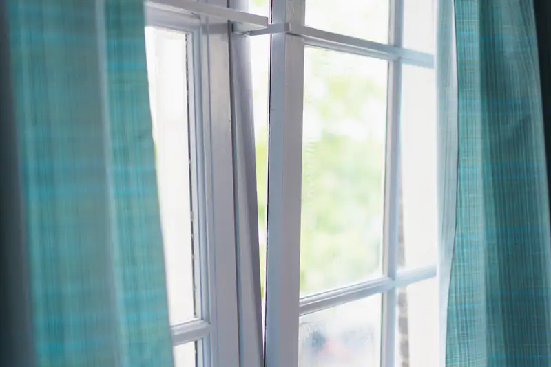 Double Glazing in Newcastle upon Tyne Open white double-glazed window framed by teal curtains, illustrating double glazing for homes in Newcastle upon Tyne