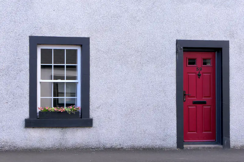 uPVC Doors in Newcastle upon Tyne White cottage with a red front door and a small sash window, illustrating uPVC doors for homes in Newcastle upon Tyne